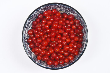 A  top-down shot of a decorative blue and white bowl filled with vibrant red currants, centered on a neutral grey background