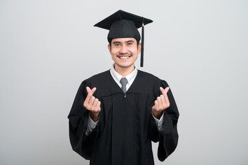 A young man in a graduation gown and cap smiles at the camera, striking a confident pose to...