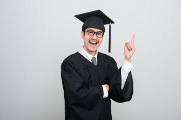 A young man in a graduation gown and cap smiles at the camera, striking a confident pose to...