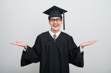 A young man in a graduation gown and cap smiles at the camera, striking a confident pose to...