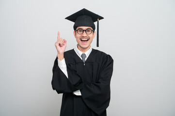 A young man in a graduation gown and cap smiles at the camera, striking a confident pose to...