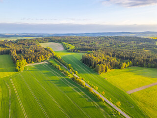 Lush green fields and forests stretch across the landscape as the sun sets on a spring evening,...