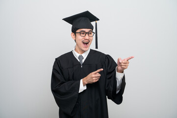 A young man in a graduation gown and cap smiles at the camera, striking a confident pose to...