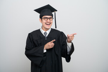 A young man in a graduation gown and cap smiles at the camera, striking a confident pose to...