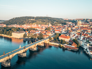 Aerial view captures Charles Bridge bathed in golden light at sunrise. Prague's historic...