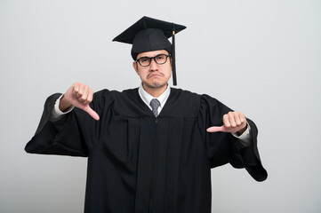 A young man in a graduation gown and cap smiles at the camera, striking a confident pose to...
