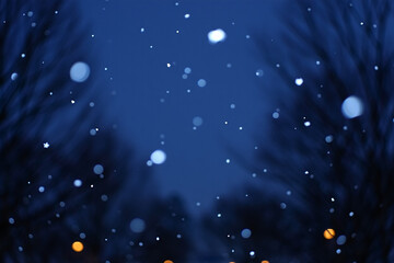 Gentle snowfall at dusk with blurred trees and distant lights creating a magical atmosphere