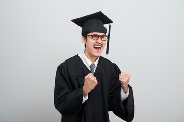 A young man in a graduation gown and cap smiles at the camera, striking a confident pose to...