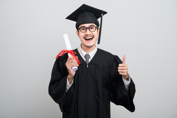 A young man in a graduation gown and cap smiles at the camera, striking a confident pose to...