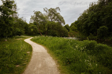 Winding path, lush greenery, overcast sky. Natural landscape, tranquil setting. Outdoor recreation,...