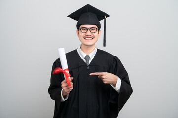 A young man in a graduation gown and cap smiles at the camera, striking a confident pose to...