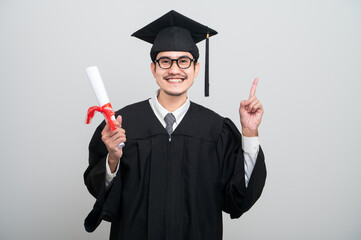 A young man in a graduation gown and cap smiles at the camera, striking a confident pose to...