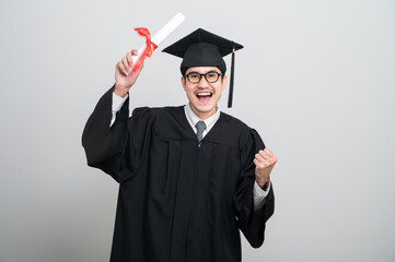 A young man in a graduation gown and cap smiles at the camera, striking a confident pose to...