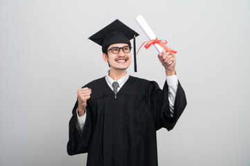 A young man in a graduation gown and cap smiles at the camera, striking a confident pose to...