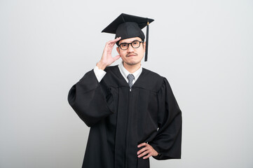 A young man in a graduation gown and cap smiles at the camera, striking a confident pose to...