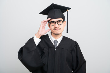 A young man in a graduation gown and cap smiles at the camera, striking a confident pose to...
