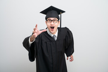 A young man in a graduation gown and cap smiles at the camera, striking a confident pose to...