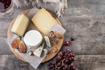 board of different cheeses with nuts, figs and grape on wooden table. Top view. Copy space
