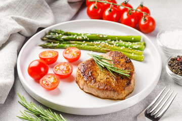 Close up, macro of tasty grilled beef steak served with green asparagus and cherry tomatoes on white plate, with cutlery. Perfect for food menu, diet, or culinary design concepts.