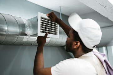 Worker installing air duct vent in a residential basement during the day