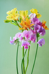Fresh bouquet of yellow alstroemeria and pink sweet pea flowers against a soft green background. Bright floral composition for spring and summer design themes