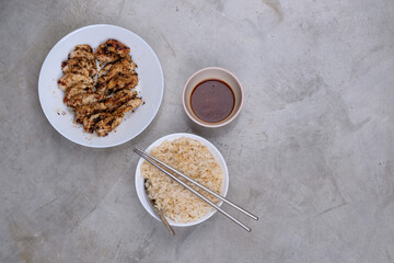 Chicken steak served with rice and dipping sauce on a raw concrete table
