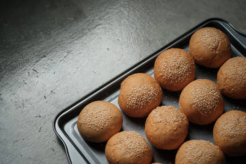 top view shot of a part of oven tray full with sesame burger buns put on rusty kitchen table with...
