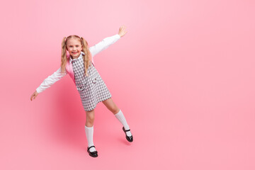 Happy schoolgirl posing against pink background wearing stylish uniform with ponytails, expressing...