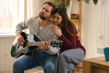 Happy couple in love dating. Man plays guitar to his girlfriend. Husband playing acoustic guitar...