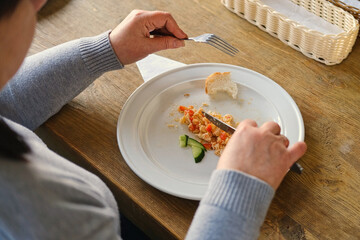 Happy senior woman eating a scramble on a white plate with vegetables. Elderly lady using knife and fork to cutting meal, has a breakfast. Balanced diet, cooking, culinary. Food concept. Old woman