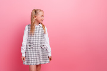 Charming schoolgirl smiling against pink background wearing stylish plaid uniform with white blouse...