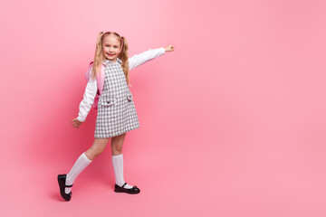 Charming little schoolgirl in a stylish uniform smiling confidently against a pink background, expressing joy