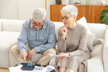 Middle aged senior couple sit with laptop and paper document. Older mature man woman reading paper...