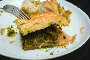 Close-up of assorted baklava desserts with pistachios on a white plate, showcasing traditional Middle Eastern and Turkish sweets in rich detail.