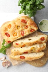 Cut delicious focaccia with tomatoes, spices and oil on gray table, flat lay