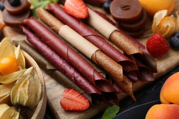 Tasty candied leather rolls, fruits and berries on wooden table, closeup