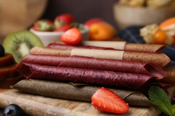 Tasty candied leather rolls, fruits and berries on wooden table, closeup