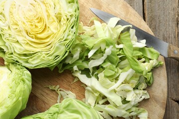 Cut cabbages and knife on wooden table, flat lay