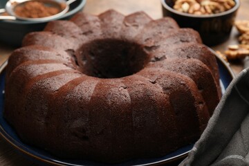 Tasty chocolate bundt cake, walnuts and cocoa powder on table, closeup