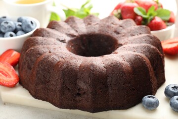 Tasty chocolate bundt cake and berries on light table, closeup