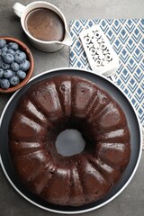 Tasty chocolate bundt cake, blueberries and server on grey table, flat lay