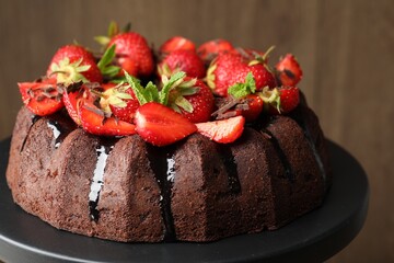 Delicious bundt cake with strawberries, mint and chocolate shavings on stand against blurred background, closeup
