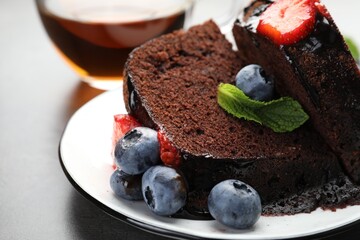 Pieces of delicious chocolate bundt cake with strawberries, mint and blueberries on grey table, closeup