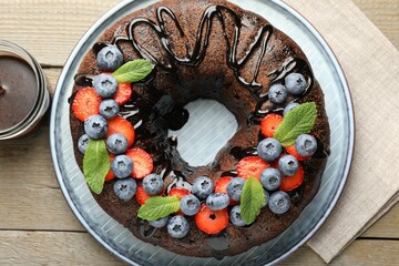 Delicious chocolate bundt cake with strawberries, mint and blueberries on wooden table, flat lay