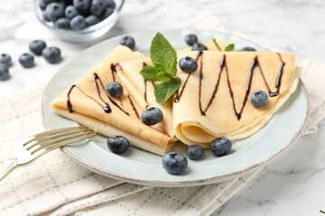 Tasty crepes with blueberries, chocolate sauce and mint served on white marble table, closeup