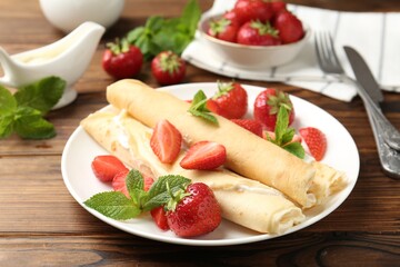 Tasty crepes with cream, strawberries and mint on wooden table, closeup
