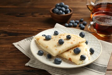 Tasty crepes with cream, blueberries and tea on wooden table, closeup