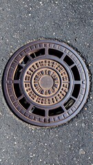 Worn Cast Iron Manhole Cover Resting On Textured Asphalt Surface Showing Circular Pattern