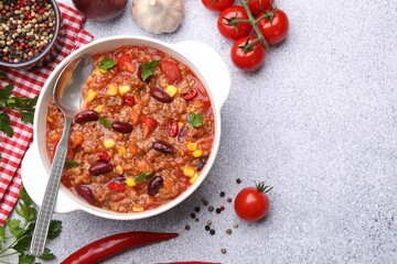 Tasty chili con carne in bowl and ingredients on grey table, flat lay. Space for text