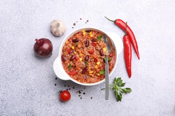 Tasty chili con carne in bowl and ingredients on grey table, flat lay